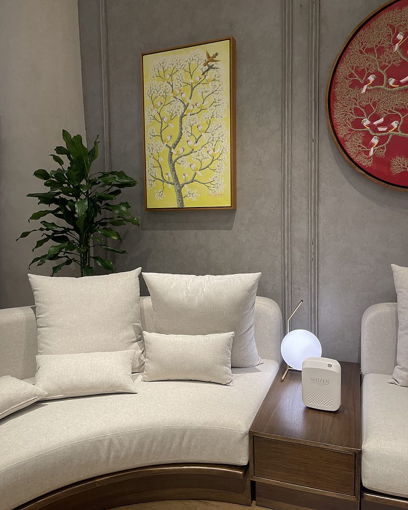 A corner of a furniture showroom with a white sofa, cream cushions, a globe lamp and a white Shizen unit on the side table