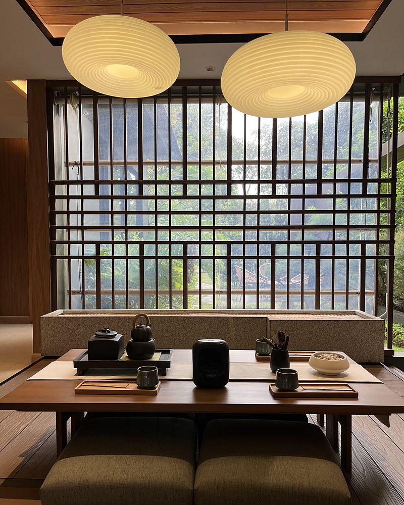 A Japanese-style living room with a timber lattice, two paper lamps, a low table with a tea set and a black Shizen unit