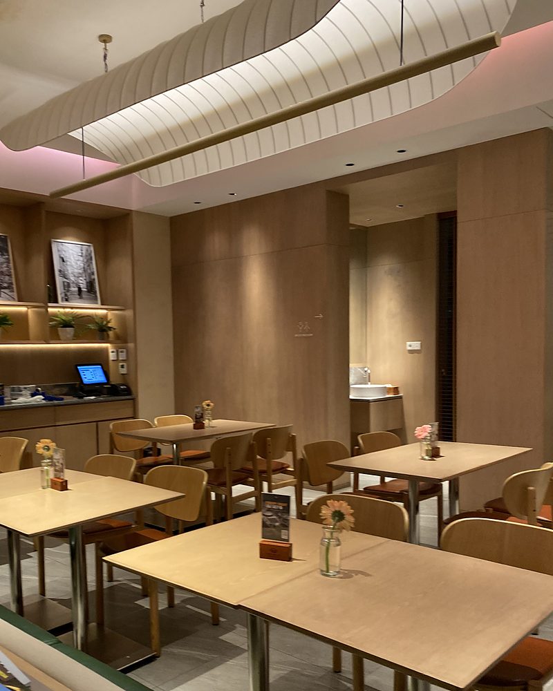 A café with timber walls, pale wooden tables, small vases of flowers and fabric pendant lamps